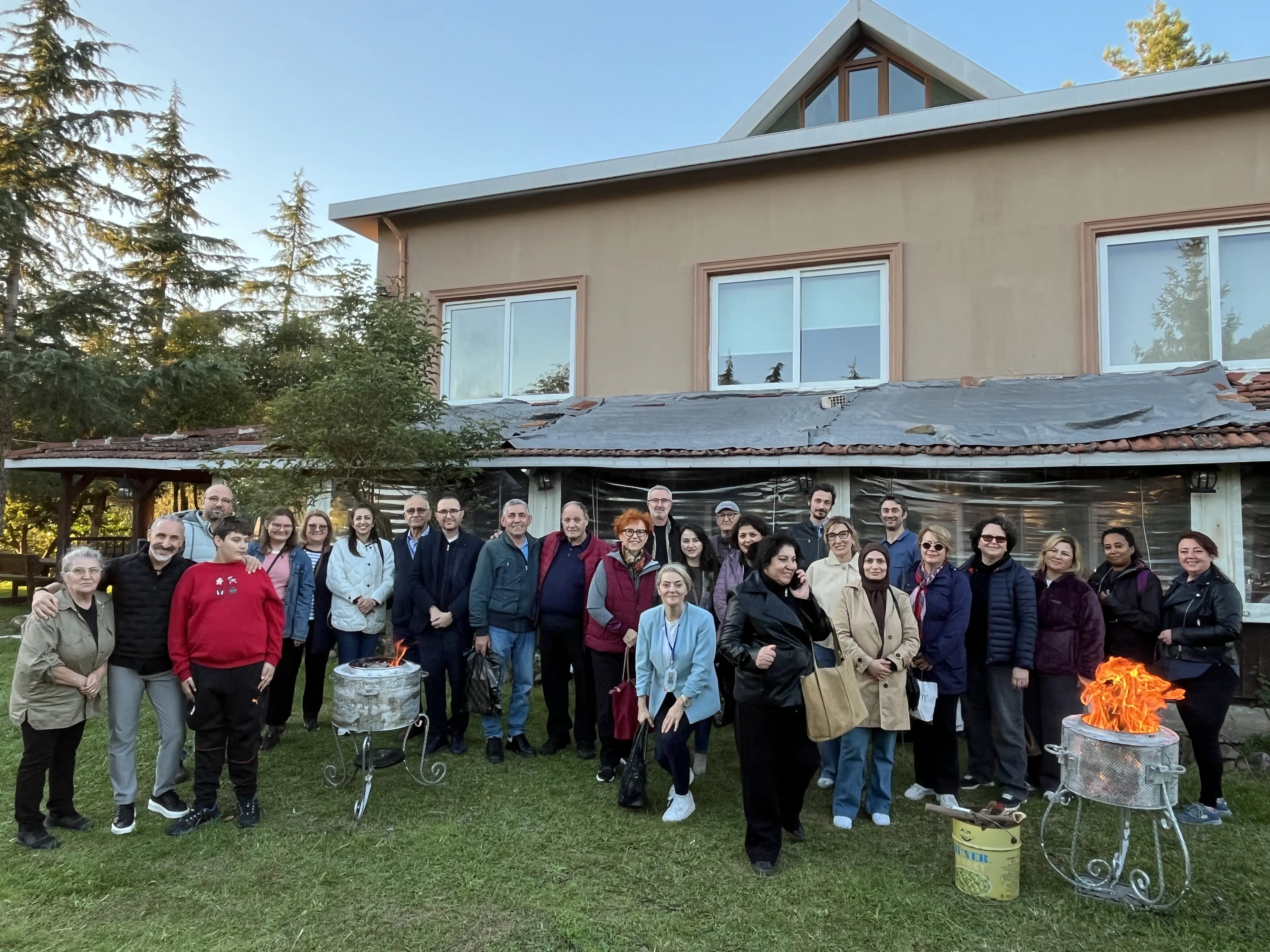 Association group gathered on a lawn in front of a house, with grills nearby